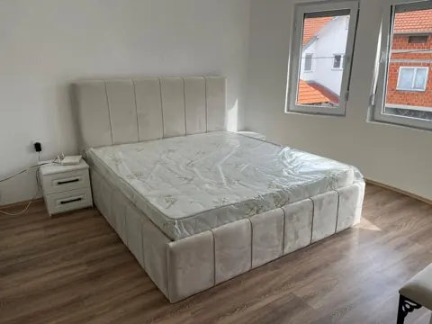 Krevat i tapetuar bezhë me kokë me kanale vertikale dhe komodinë të bardhë