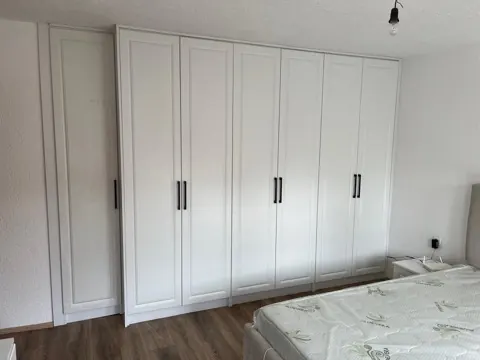 Dollap i bardhë me kornizë nga muri në mur në dhomë gjumi