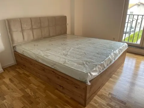 Krevat me kokë të tapetuar bezhë dhe kornizë nga lisi me hapësirë ruajtjeje